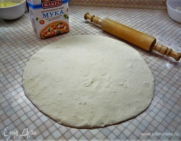 Выкладываем тесто на посыпанный мукой стол и раскатываем его в круглый пласт.