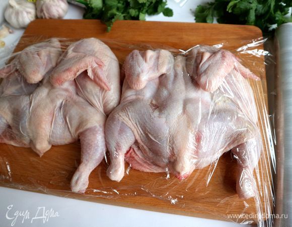 Перевернуть цыплят грудкой вниз, покрыть пищевой пленкой, отбить слегка, стараясь не повредить трубчатые кости. Я приподнимаю крылышко, отбиваю немного грудку цыпленка и другие части. Цыпленок должен стать более плоским. Если работают мужчины, то им зачастую кухонный молоток не требуется, они расправляют птицу и приминают руками.