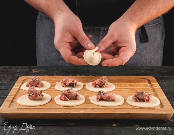 Выложите в центр заготовки фарш, сложите заготовку вдвое и тщательно защипните края, соедините «ушки». Повторите процедуру с каждой заготовкой. Накройте пельмени полотенцем, чтобы они не подсохли. Затем отварите необходимое количество пельменей (часть можно заморозить впрок).