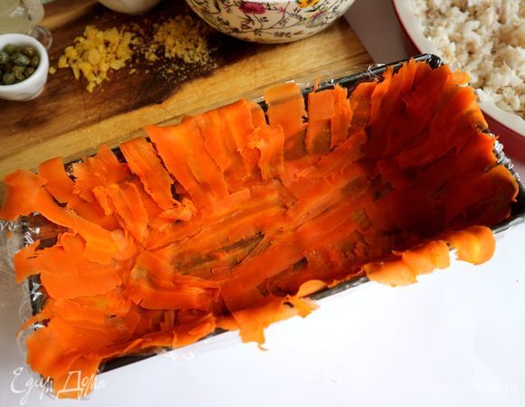 Прямоугольную форму смазать слегка сливочным маслом, застелить пищевой пленкой. С моркови снять тонкие пластины с помощью овощечистки. Дно и боковые части формы покрыть тонкими пластинами из моркови.