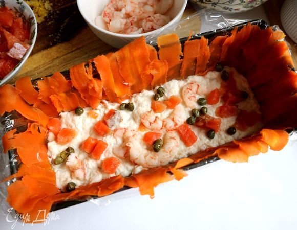 Нижний слой — часть измельченной в блендере трески, которую следует выложить равномерно на дно формы. Затем — кусочки красной рыбы, часть креветок, несколько каперсов, вяленые в масле помидоры, часть цедры, измельченной крупно.