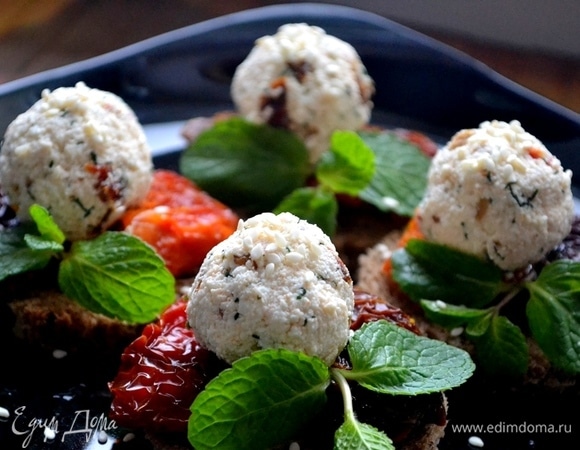 На каждый ломтик кладем по 2 вяленых томата, сверху поливаем оливковым маслом (буквально несколько капель). Кладем сырные шарики, украшаем зеленью, посыпаем кунжутом и подаем к столу. Закуску можно сделать заранее, она прекрасно стоит в холодильнике.