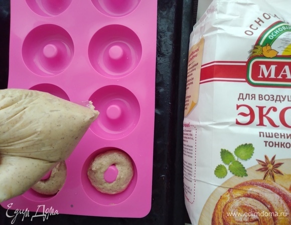 Приготовить формочки для пончиков. Если у вас, как у меня, силиконовые — смазывать не нужно, если тефлон — смазать сливочным маслом. Распределить тесто с помощью кондитерского шприца или пакета с обрезанным краем. Так получаются ровненькие экземпляры.
