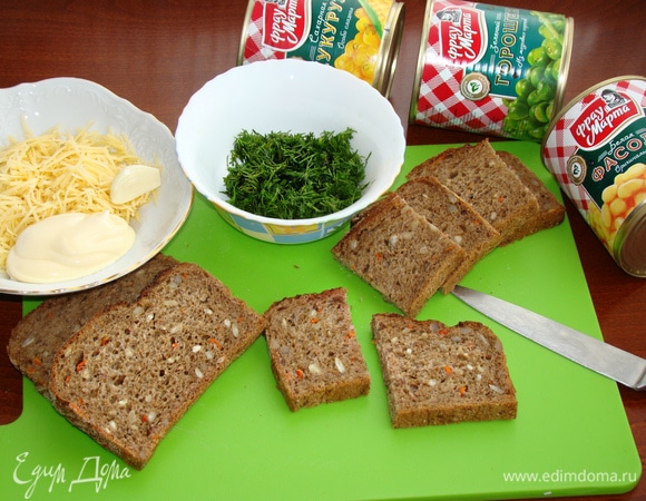 Теперь займемся зеленой «полянкой» для наших поросят. Для этого ломтики хлеба разрезать пополам. Сыр натереть на мелкой терке, к нему добавить зубчик чеснока, пропущенного через пресс, 3 ст. л. майонеза и перемешать. Зелень укропа мелко нашинковать. Хлеб можно взять любой по вкусу. У меня хлеб злаковый, потому что мне кажется, что такая основа-полянка будет еще вкуснее.