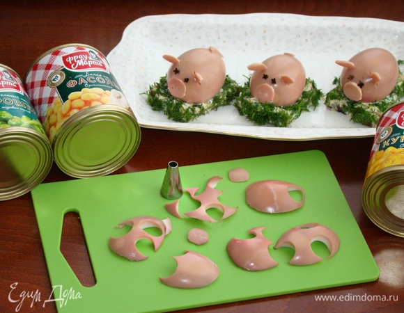 Из оставшихся «брюшек» вырезаем пятачки, ушки и хвостики и с помощью майонеза закрепляем на свинках. Глазки можно сделать из гвоздики или черного перчика. Готовых свинок укладываем на полянки.