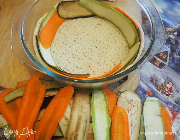 В смазанную масло огнеупорную круглую форму укладываем готовый корж для пиццы. Потом начинаем поочередно по кругу выкладывать наши овощи внахлест.