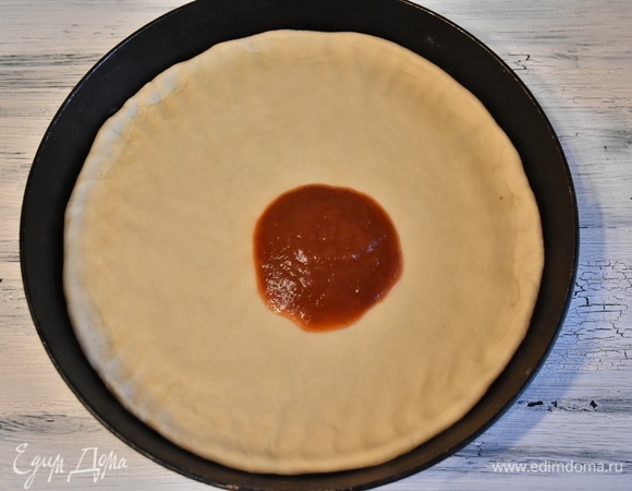 Тесто смазать любым томатным соусом. Поставить сковороду на плиту на средний огонь. Моя пицца начала уже готовиться, и я постепенно добавляю компоненты начинки. На этом этапе уже можно включить разогреваться духовку.
