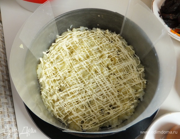 Берем круглую форму, ставим ее на блюдо. Борта формы закрываем специальным воротником. Укладываем в форму слой тертого картофеля, делаем майонезную сеточку из оливкового майонеза ТМ «МахеевЪ».
