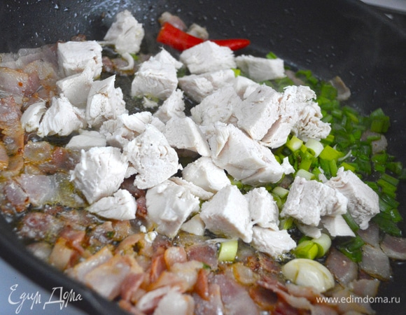 Предварительно отварить куриную грудку, бульон не выливать. В сотейнике обжарить бекон, добавить лук зеленый, зубчик чеснока, нарезанный острый перец и нарезанную кубиками грудку, слегка обжарить.