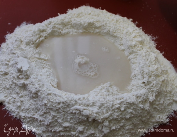 К муке добавьте воду с растворенными в ней дрожжами и начните замес теста.