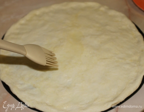 Отделите кусочек теста и сформируйте тонкую основу для пиццы с бортиком по краю. Смажьте основу оливковым маслом.