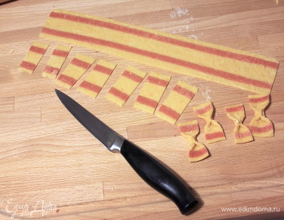 Затем нарезаем тесто на полоски шириной 3–4 см, а из полосок нарезаем прямоугольники размером примерно 4х2 см. Если есть дисковый нож с мелкими зубчиками, то можно делать заготовки с его помощью — получится красиво. Формируем из заготовок бантики.