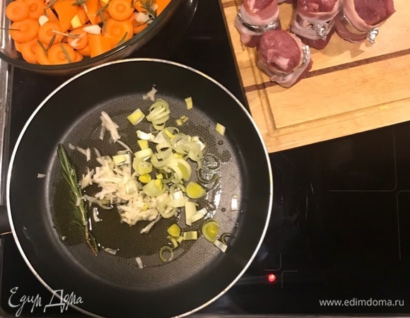 В форму для запекания выкладываем нарезанную колечками морковь. На сковороде с оливковым маслом и веточкой розмарина обжариваем давленый чеснок, нарезанный полукольцами лук-порей. Выкладываем на морковь.