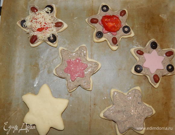 На противень, застеленный силиконовым ковриком и пергаментом, выложить заготовки из теста, дать им постоять в теплом месте 15 минут, потом смазать их измельченной смесью, положить кусочек колбасы, помидора, украсить фасолью и кружочками маслин и посыпать тертым сыром. Отправляем в разогретую до 180°C духовку минут на 15–20.