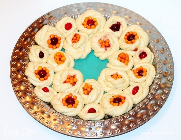 Даем тесту немного подойти под пленкой, а лучше — под пакетом. Затем у каждой заготовки аккуратно приминаем серединку, кладем немного джема (0,5 ч. л.), а затем — ягоды. Крупную ягоду лучше обмакнуть во взбитое яйцо, а затем выложить в середину веночка.