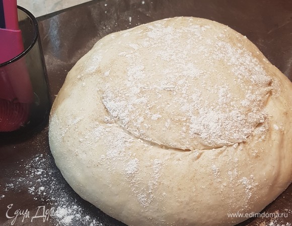 Каравай переложить на коврик для выпечки. В 1 столовой ложке воды растворить соль (на кончике ножа) и соду (на кончике ножа). Этой смесью при помощи кисточки смазать наш каравай, посыпать мукой (как бы припудрить). Сделать полукруглый надрез. Поставить выпекаться на 45 минут.