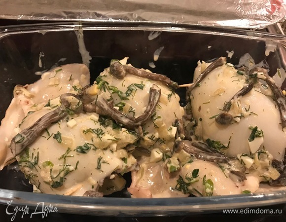 Фаршируем грибами тушки кальмаров. Скрепляем зубочисткой края. Оставшуюся начинку распределите по поверхности, смажьте сметаной и отправьте в духовку на 30 минут при 180°C до образования румяной корочки.
