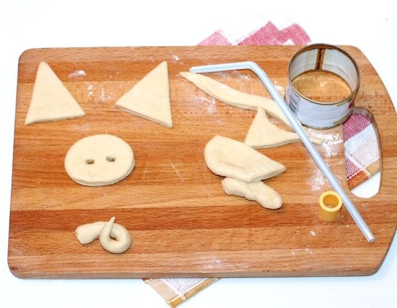 Из раскатанного кусочка теста (40 г), вырезаем ушки, хвостик и пятачок. Из маслин вырезаем глаза.