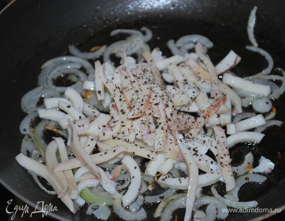 К обжаренному луку добавить кальмар, нарезанный соломкой, добавить черный перец по вкусу и обжарить все вместе минуту.
