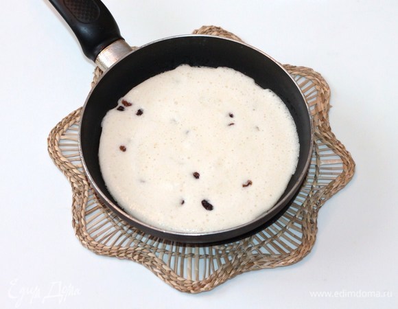 На сковородке разогреть сливочное масло, вылить туда половину теста и посыпать 50 г промытого изюма.