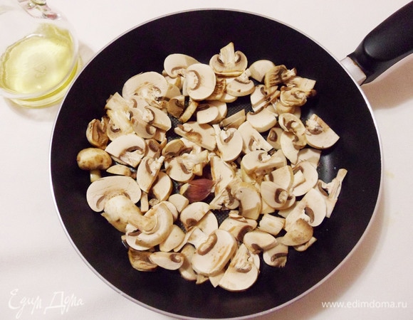 Зубчик чеснока раздавить ножом. Разогреть в сковороде ложку оливкового масла, добавить чеснок. Как только почувствуете аромат чеснока, добавьте в сковороду шампиньоны.