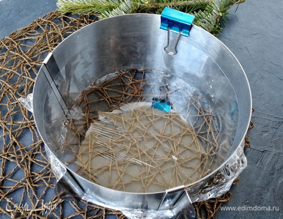 Теперь надо залить этим муссом заготовку, которая стоит в морозилке. Для этого берем раздвижное кулинарное кольцо и выставляем диаметр 18,5 см. Низ обтягиваем пищевой пленкой. Чтобы она лучше прилипла, смочите внешнюю часть кольца водой. Внутреннюю часть кольца прокладываем ацетатной лентой высотой 5 см. Чтобы она хорошо прилипла, также смочите бортик водой. Стык ленты я закрепила зажимом, чтобы лента случайно не свернулась и никуда не сбежала.