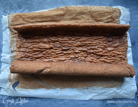 Достать бисквит. Сверху на корж разложить чистое кухонное полотенце и вместе с бумагой и полотенцем свернуть бисквит в рулет. В таком виде дать ему полностью остыть.