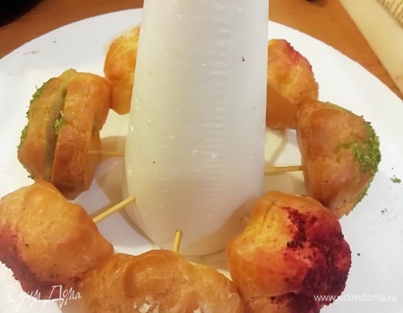 Приступаем к сборке нашей елочки. Основу можно скрутить из картона или использовать готовый конус из пенопласта. Обрезаем деревянные шпажки, втыкаем в основание и насаживаем профитроли.