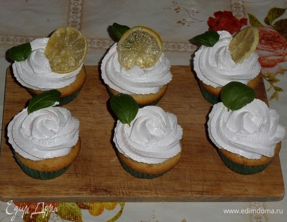 Готовим крем. В чашку выкладываем яичные белки. Добавляем 110 г сахара. Чашку с белками и сахаром ставим на водяную баню и начинаем взбивать массу с помощью миксера. Взбиваем до устойчивых пиков и увеличения объема массы в течении 5–7 минут. Затем убираем чашку с водяной бани и взбиваем крем еще 3–4 минуты. Наполняем кремом кондитерский мешок и украшаем кексы. Затем украшаем листиками мяты и ломтиками лимона.