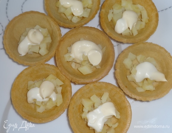 В каждую тарталетку выложить по чайной ложке майонеза, распределить его по картофелю. Сверху выложить горошек, рыбу, икру, огурцы, посыпать зеленым луком.