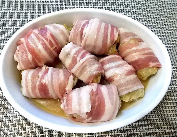 Заверните каждый голубец в полоску бекона и уложите в форму для запекания. Полейте их жидкостью из сковороды, где тушились голубцы.