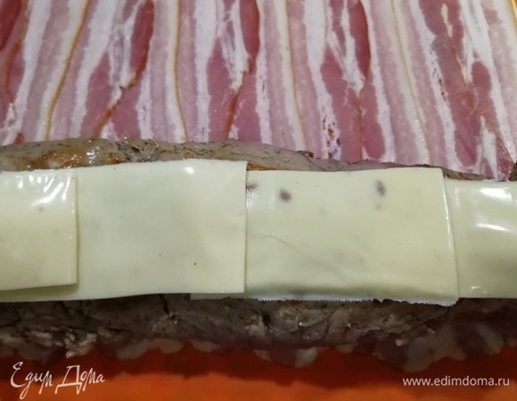 На один край бекона выкладываем вырезку швом вверх и закрываем его полосками плавленого сыра. Оборачиваем вырезку беконом при помощи силиконового коврика.