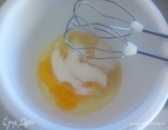 Подготовим продукты. Для приготовления торта нужно будет испечь 3 бисквитных коржа. Для 1 коржа потребуется 2 яйца, 90 гр. сахара, 1 ч. л. ванильного сахара, 70 г муки, 1/2 ч. л. разрыхлителя, 2 ст. л. растительного масла, 2 ст. л. кипятка. Диаметр формы 20 см. На дно формы кладем пергамент. В чашу миксера выкладываем 2 яйца и 90 г сахара.