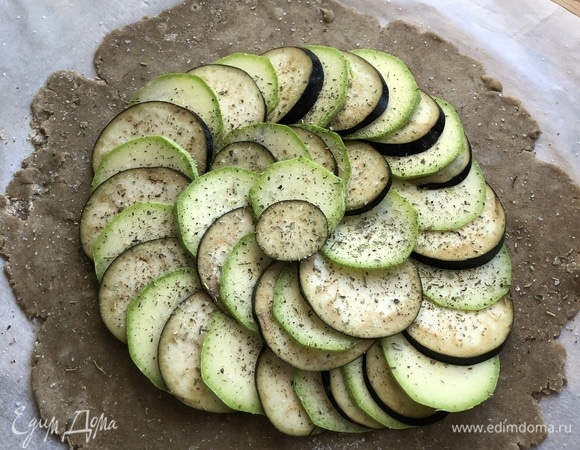 Выложите овощи на тесто отступая 2 см от края. Посыпьте начинку травами.