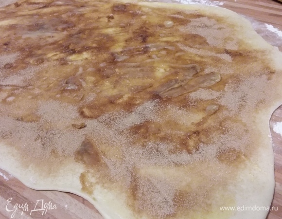 Подошедшее тесто обмять и на посыпанной мукой поверхности раскатать в прямоугольник размером приблизительно 60х30 см. Смазать растопленным и охлажденным сливочным маслом и посыпать смесью сахара и корицы.