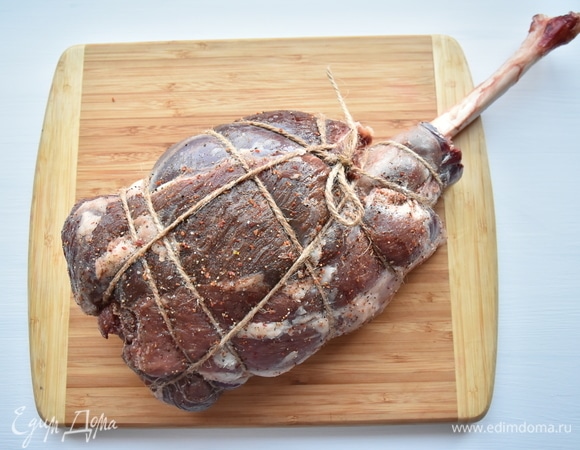 Нашпиговать баранью ногу зубчиками чеснока. Сбрызнуть оливковым маслом, посолить, обсыпать смесью свежемолотых перцев. Хорошенько руками распределить специи по всей поверхности куска. Ногу обвязать бечевкой, чтобы мясо при запекании держало форму. Зафиксировать берцовую кость.