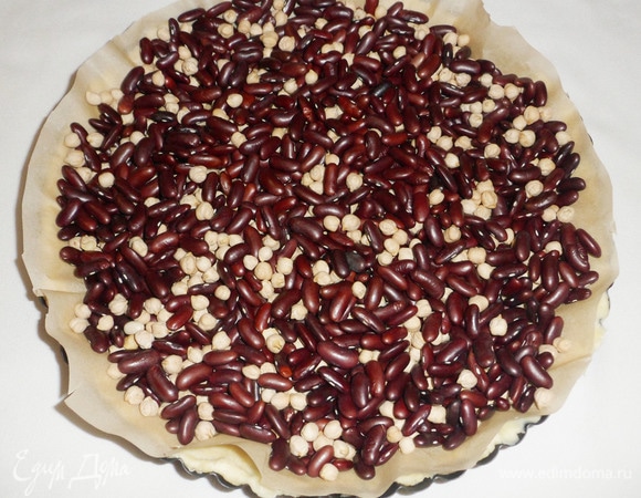 Чтобы тесто при выпечке не вздувалось и чтобы бортики не сползли вниз, необходимо застелить тесто пергаментной бумагой для выпечки и высыпать груз (у меня смесь фасоли с горохом). Поставить в разогретую до 180°C духовку на 20–25 минут (ориентируйтесь по своей духовке).