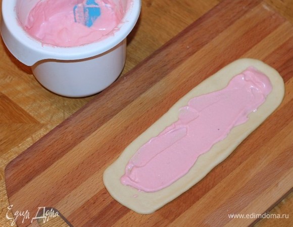 Припыляем разделочную доску мукой (небольшая щепотка). Достаем по одной заготовке и раскатываем тесто по форме овальной лепешки размером примерно 10х22 см. Смазываем лепешку кремом (2 ч. л.). Край лепешки не смазываем кремом. При выпечке крем не растекается благодаря яичному белку.