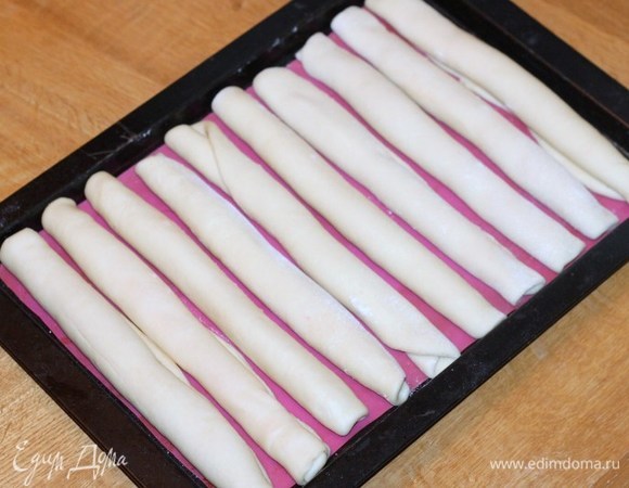 Форму для выпечки (22х33 см) застелите пекарской бумагой и смажьте маслом. Силиконовый коврик не смазываем маслом. Раскладываем рулетики на противне и оставляем между ними небольшой промежуток для роста теста (1–2 см). Накрываем противень легким сухим полотенцем и даем время увеличиться заготовкам (примерно 30 минут).