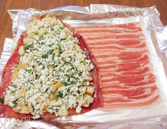 Форму для запекания застелить фольгой, выложить ломтики бекона так, чтобы они немного заходили друг на друга. Затем на бекон уложить развернутое филе горбуши так, чтобы рыба прикрыла не больше половины бекона. Затем на рыбу равномерно выложить творожную начинку.