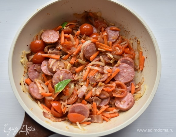 Краковскую колбасу нарезать кружочками и добавить к овощам с беконом. Перемешать, немного обжарить все вместе. Вместо краковской колбасы можно взять охотничьи колбаски.