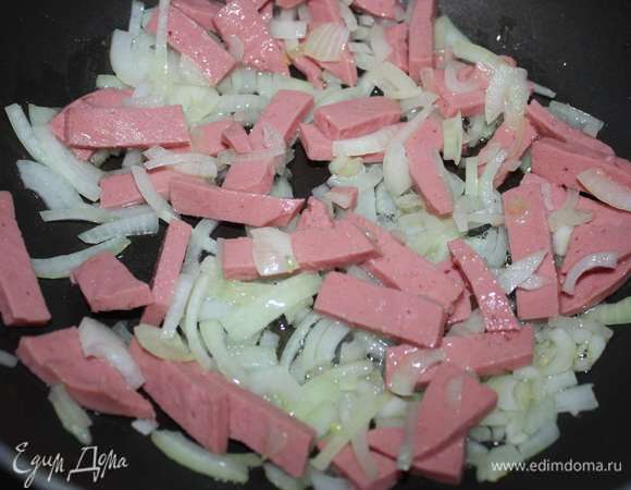 Колбасу нарезать и выложить на сковороду к луку, жарить еще 2 минуты.