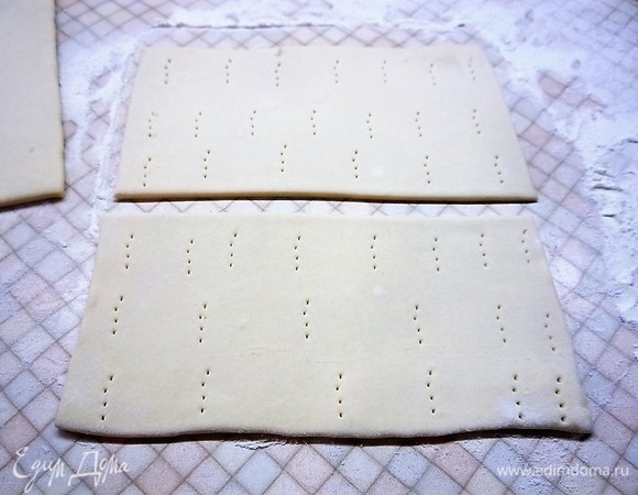 Пласты слоеного теста слегка раскатываем, делим каждый пополам и накалываем вилкой.