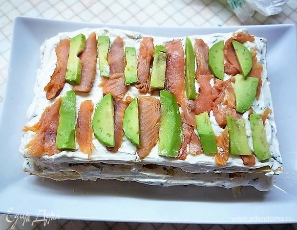 Затем укладываем еще один корж, смазываем кремом, укладываем ломтики рыбы и авокадо.