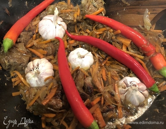 Выложите очищенный от шелухи чеснок и перец чили. Перец не даст остроту блюду. При желании перец можно выдавить в готовый плов.