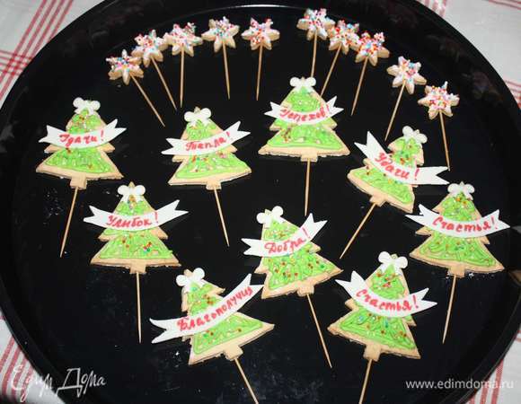 На елочки поместить надписи с пожеланиями. Сверху елочки украсить бантиками из мастики. Елочки и звездочки украсить цветной кондитерской посыпкой.