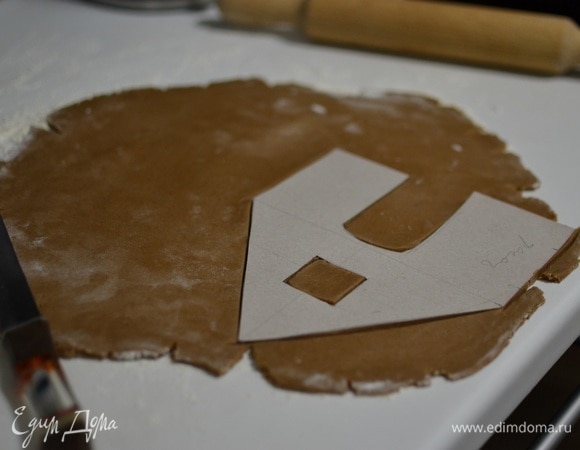 Из картона нужно вырезать заготовки для пряничного домика. Можно найти на просторах интернета уже готовые шаблоны или придумать модель самостоятельно. Достать тесто из холодильника, раскатать, вырезать нужные фигуры для домика по шаблону. Выпекаем составляющие домика порядка 8–10 минут при 180°C. Свежеиспеченные заготовки сначала будут мягкими, но потом очень быстро затвердеют.