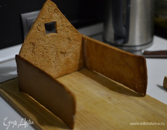 Когда все составляющие детали будут полностью готовы, приступаем к сборке пряничного домика. Окунаем части домика торцом в горячую карамель и быстро скрепляем между собой. Сначала склеиваем боковую стену и фасад, потом прикрепляем вторую боковую сторону и заднюю стенку дома. Работать нужно быстро, так как карамель очень быстро застывает. В самую последнюю очередь крепим крышу. Оставляем сформированный домик примерно на час.