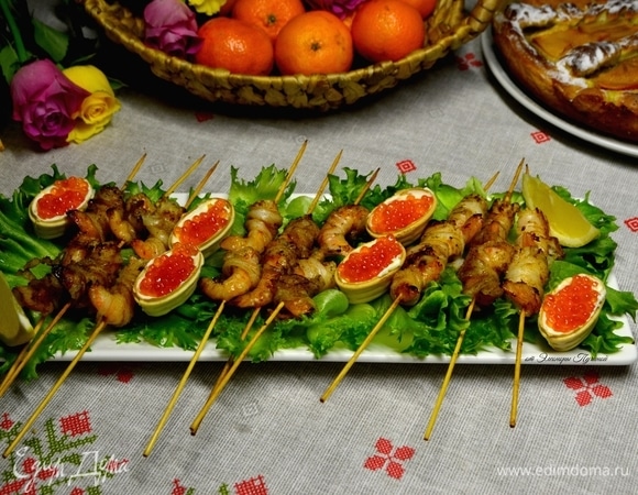 Большое блюдо украсить листьями салата, креветки на шпажках выложить на листья, рядом положить тарталетки, наполненные маскарпоне и красной икрой, и дольки лимона. Соком лимона сбрызнуть креветки. Вкусная праздничная закуска готова!