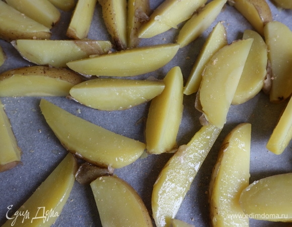 Картофель тщательно вымыть, отварить в мундире почти до готовности. Слить воду. Нарезать на ломтики, положить в кастрюлю, посолить, посыпать гранулированным сухим чесноком, сбрызнуть оливковым маслом, перемешать. Противень застелить бумагой для выпечки. Положить картофель в один слой. Поставить в духовку на нижний уровень на 25–30 минут.